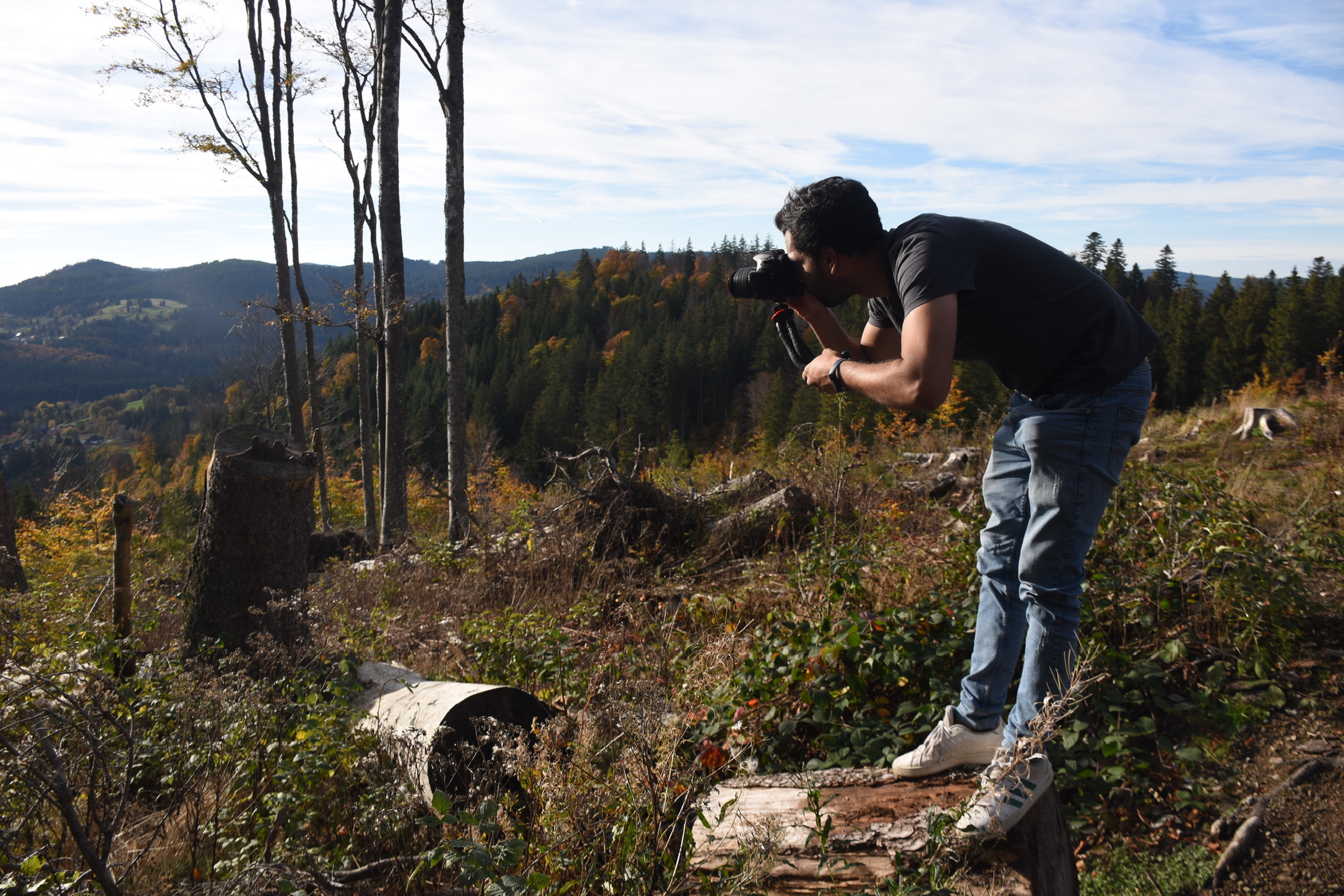 Esas Khan photographing a mountain forest, camera raised to his eye.